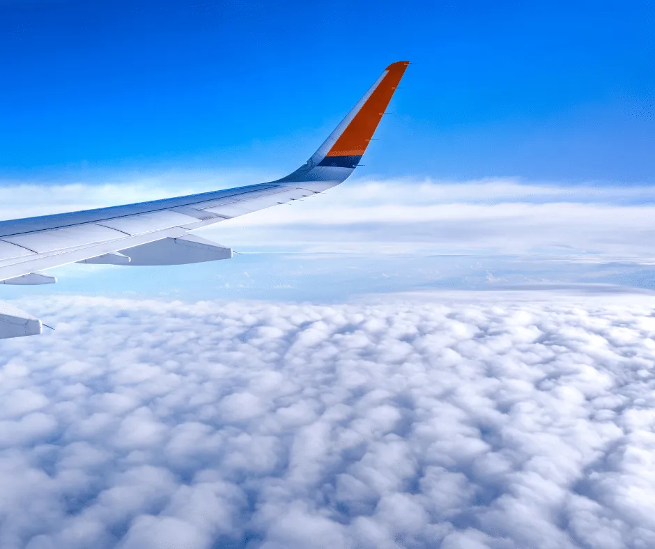 Aile d'avion au-dessus des nuages illustrant le transport aérien du défunt organisé par les Pompes Funèbres Hennard