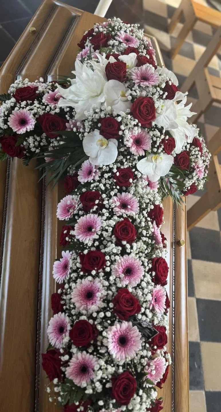 Composition florale et croix posées sur un cercueil lors d'obsèques organisées par les Pompes Funèbres Hennard
