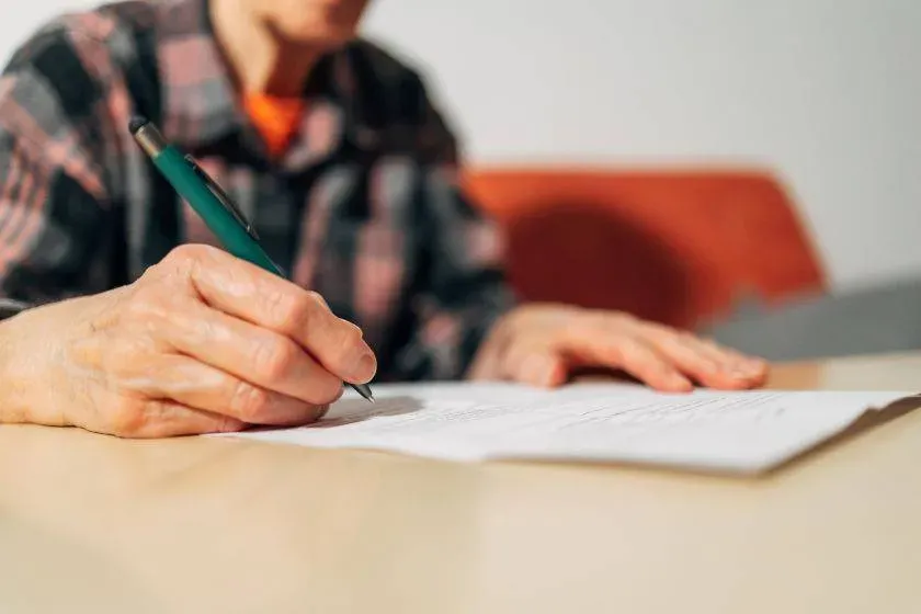 Personne âgée signant un document pour organiser sa prévoyance obsèques.