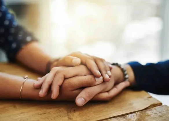 Mains enlacées posées sur une table en bois en signe de soutien.