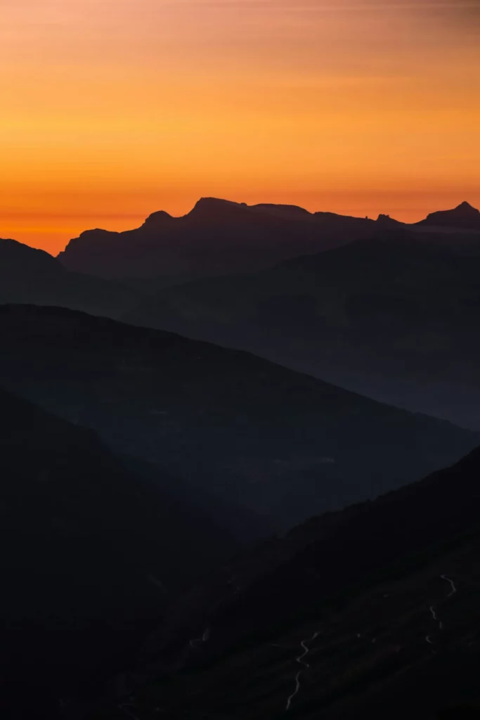 Silhouette de montagnes sombres sous un coucher de soleil orange.